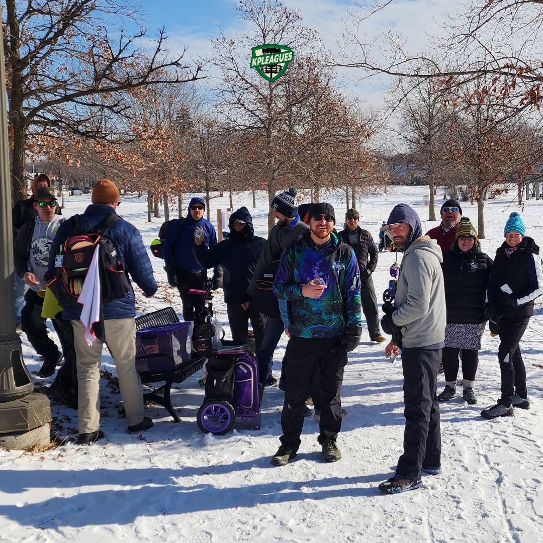 Disc golfers gathered with their bags on a snow-covered course.