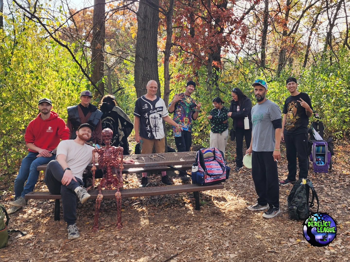 Disc golfers gathered around a picnic table on a wooded course in autumn.